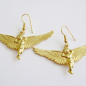 K&ouml;nnte beinhalten: Goldfarbene Ohrringe mit einem Cherub mit Fl&uuml;geln. Der Cherub h&auml;lt sich den Kopf in der Hand und hat ein zartes, detailliertes Design.
