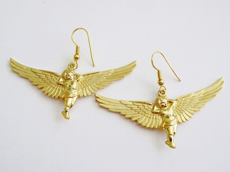 K&ouml;nnte beinhalten: Goldfarbene Ohrringe mit einem Cherub mit Fl&uuml;geln. Der Cherub h&auml;lt sich den Kopf in der Hand und hat ein zartes, detailliertes Design.