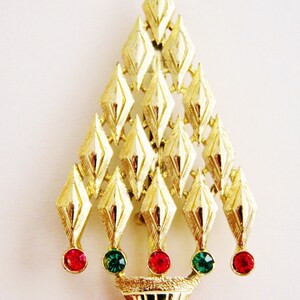 May include: A gold-tone Christmas tree brooch with red and green rhinestones. The tree is made of a series of overlapping diamond shapes.