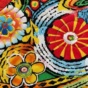 May include: Close-up of a vibrant, quilted fabric with a floral pattern. The design features large, stylized flowers in red, yellow, and orange, set against a black background. The quilting stitches are visible in gold thread, adding texture and detail.