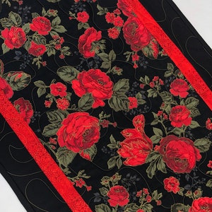 May include: A black table runner with red and gold floral print. The runner has a red and gold trim.