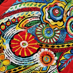 May include: Close-up of a vibrant, quilted fabric with a colorful floral pattern. The design features red, yellow, blue, green, and black elements. The quilting stitches are visible, adding texture to the textile. The edges are framed with a red border.