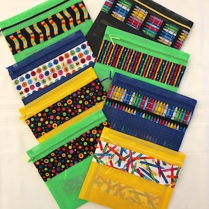 May include: A set of seven mesh zippered bags with different colorful patterns. The patterns include alphabet letters, polka dots, crayons, and stripes. The bags are made of a clear mesh material with a bright green border and a yellow zipper.