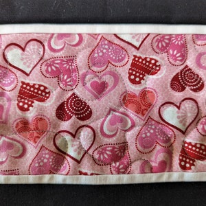 May include: A pink fabric with a white border and a quilted pattern of hearts in various shades of pink and red.