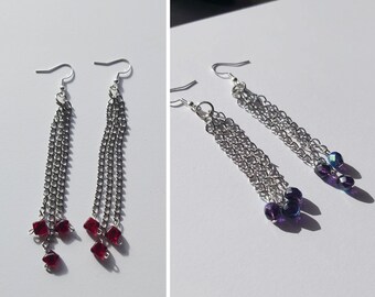 May include: Two pairs of dangle earrings with silver chains and colored beads. One pair has red beads and the other has purple beads.