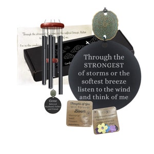 May include: A black wind chime with a wooden top and a round black plaque with the text "Through the STRONGEST of storms or the softest breeze listen to the wind and think of me". The plaque is attached to the wind chime with a metal ring. There is a small round plaque with the text "Gene Beloved Husband, Father and Friend" and a small packet of wildflower seeds with the text "Thoughts of You Will Forever Bloom Memorial Seed Flowers".