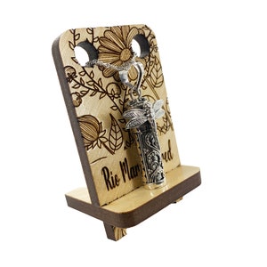 May include: A silver pendant necklace with a dragonfly design and an engraved cylinder charm. The necklace is displayed on a wooden stand with a floral design and the text "Rio Manured".