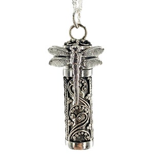 May include: Silver necklace with a dragonfly pendant. The pendant is a small cylinder with an intricate design and a dragonfly on top. The chain is a silver curb chain.