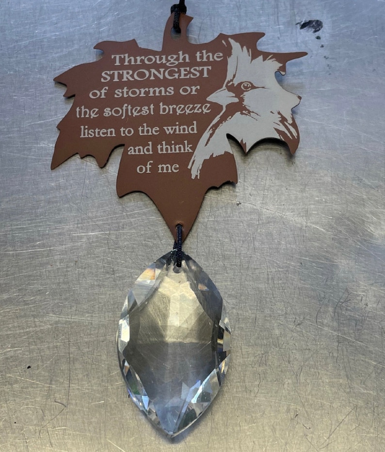 May include: A brown leaf-shaped metal ornament with a bird design and the text "Through the STRONGEST of storms or the softest breeze listen to the wind and think of me". A clear crystal prism hangs from the ornament.