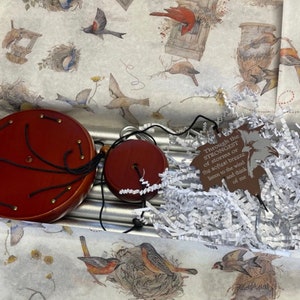 May include: A silver wind chime with wooden top and bottom pieces. The chime is packaged in a box with white tissue paper and a brown tag with the text "Through the STRONGEST of storms or the softest breeze listen to the wind and think of me".