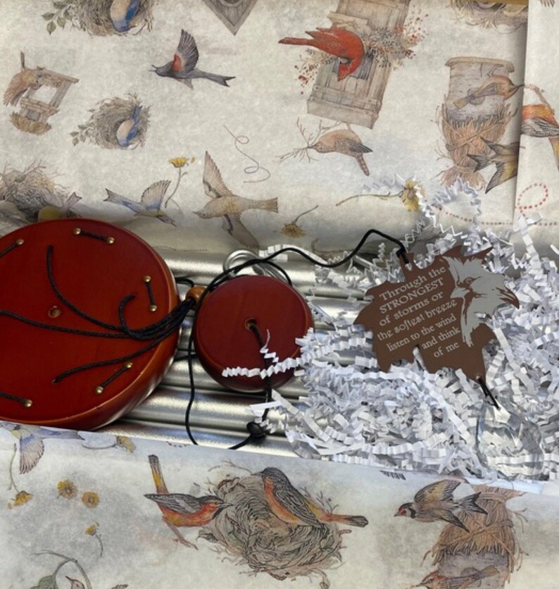 May include: A silver wind chime with wooden top and bottom pieces. The chime is packaged in a box with white tissue paper and a brown tag with the text "Through the STRONGEST of storms or the softest breeze listen to the wind and think of me".