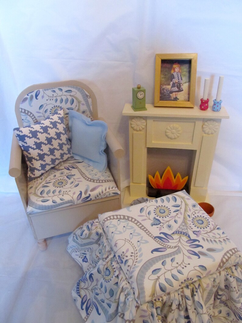 Pu&ograve; includere: Una poltrona bianca con un cuscino a motivi blu e bianchi e un cuscino blu. La poltrona &egrave; davanti a un camino bianco con un camino decorativo e una cornice con l'immagine di una ragazza con un vestito blu. Il camino ha un fuoco rosso e bianco.