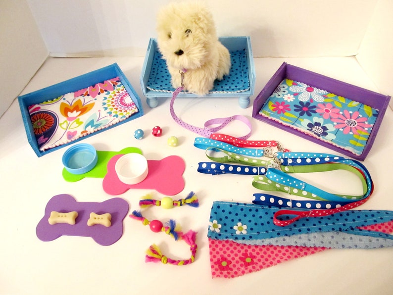 May include: A set of dog accessories for a small dog, including two blue and purple dog beds, two pink and green bone-shaped food and water bowls, a white plush dog, a blue and white lead, and a variety of colourful dog toys.