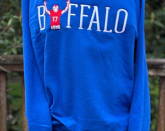 Könnte beinhalten: Ein königsblaues Sweatshirt mit Rundhalsausschnitt und weißer Stickerei, die das Wort BUFFALO bildet. Der Buchstabe U ist durch eine Stickerei eines Footballspielers im roten Trikot mit der Nummer 17 ersetzt, der die Arme hebt.