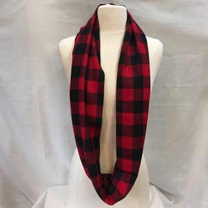 K&ouml;nnte beinhalten: Ein roter und schwarzer karierter Infinity-Schal. Der Schal ist aus einem weichen, bequemen Stoff gefertigt und perfekt, um sich im Winter warm zu halten.