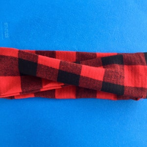 May include: Red and black plaid headband. The headband is folded in half and is lying on a blue surface.