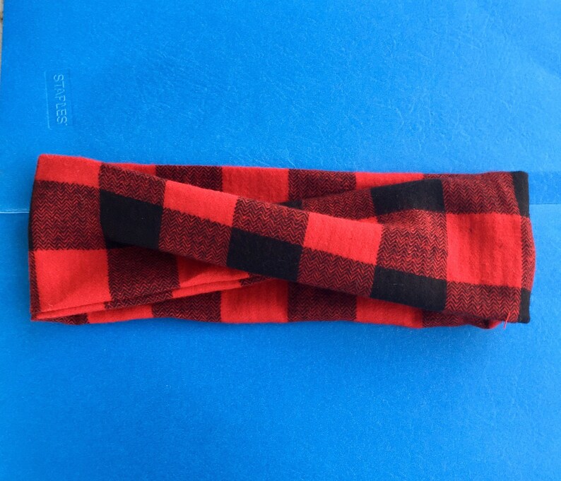 May include: Red and black plaid headband. The headband is folded in half and is lying on a blue surface.