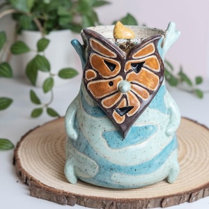 May include: A set of three ceramic mugs with a speckled, matte finish. The mugs are in shades of cream, light gray, and dark gray. Each mug has a simple, minimalist design and a rounded handle.