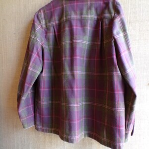 Puede incluir: Una camisa chaqueta a cuadros morados, verdes y rosas cuelga de una percha blanca. La parte trasera de la chaqueta es visible, mostrando el cuello, los pu&ntilde;os abotonados y un canes&uacute; plisado en la espalda. El estampado de cuadros es un dise&ntilde;o cl&aacute;sico.