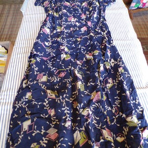 May include: A long, navy blue dress with a geometric print featuring pink, green, and white shapes. The dress has short sleeves and a V-neck.