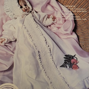 May include: A vintage sewing pattern for a Victorian gown, labeled "Robe Victorienne," for a newborn. The pattern includes instructions and is from 1980. The gown is white with lace and smocking details, and the image includes a doll.
