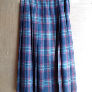 May include: A long, pleated skirt in a classic tartan pattern. The skirt features a navy blue base with a red and teal plaid design. The skirt is hanging on a hanger.