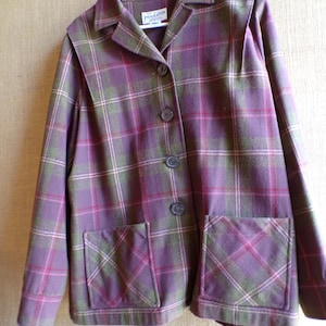Puede incluir: Una chaqueta a cuadros morada, verde y rosa con dos bolsillos delanteros y tres botones. La chaqueta tiene cuello y est&aacute; colgada de una percha blanca. La etiqueta de la marca "Pendleton" es visible.