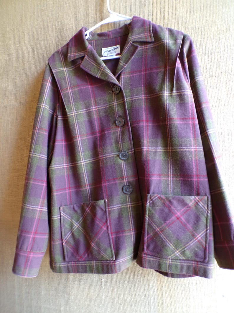 Puede incluir: Una chaqueta a cuadros morada, verde y rosa con dos bolsillos delanteros y tres botones. La chaqueta tiene cuello y est&aacute; colgada de una percha blanca. La etiqueta de la marca "Pendleton" es visible.