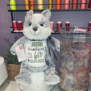 May include: A gray and white plush bear with a personalized embroidered bib. The bib reads "BRIAN Michael Ferrell III 19 1/2 inches 6.31 pounds 10-48.5 oz 02-25-2022".
