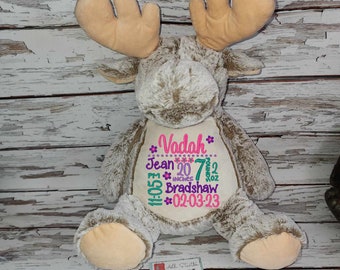May include: A plush moose toy with embroidered details. The moose is light brown with tan antlers and feet. The belly features embroidered text: "Vadah", birth details including weight 7.2 oz, length 20 inches, and date 02-03-23.
