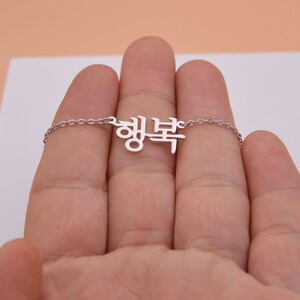 Pu&ograve; includere: Una collana d'argento con un ciondolo a forma di parola coreana. Il ciondolo &egrave; in metallo e ha uno stile delicato e corsivo.