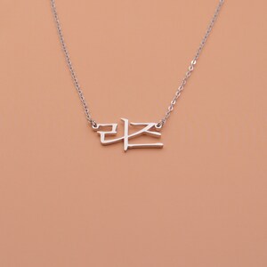 Pu&ograve; includere: Collana d'argento con un ciondolo a forma di parola coreana. La parola &egrave; "라온", che significa "gioia" in coreano.