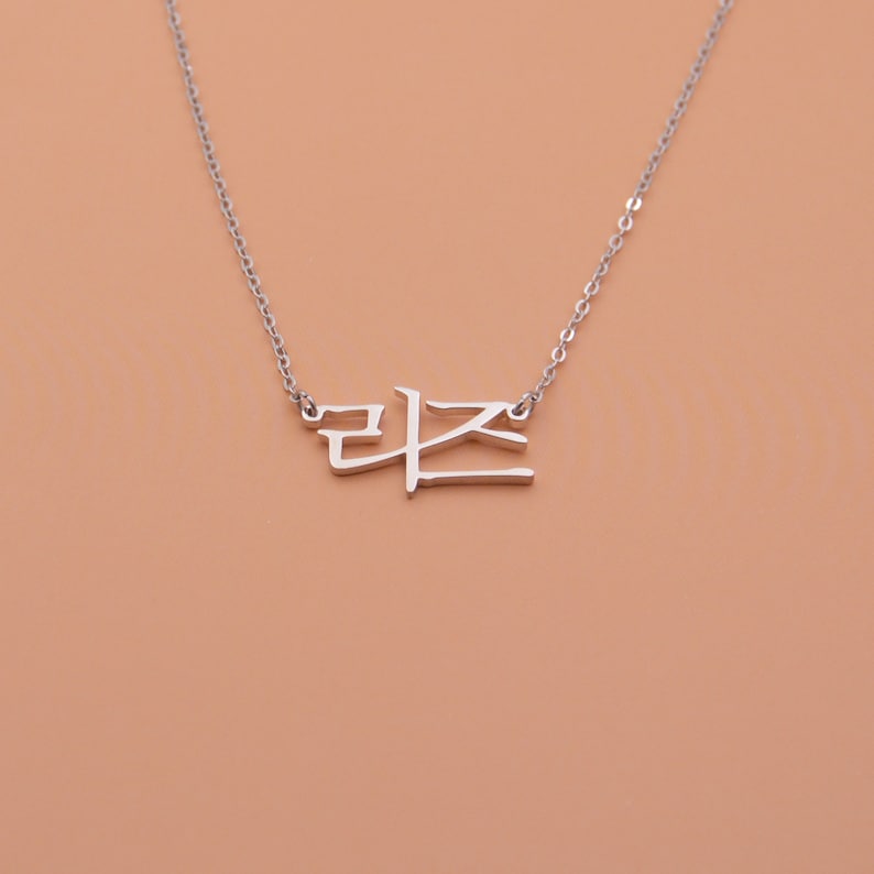Pu&ograve; includere: Collana d'argento con un ciondolo a forma di parola coreana. La parola &egrave; "라온", che significa "gioia" in coreano.