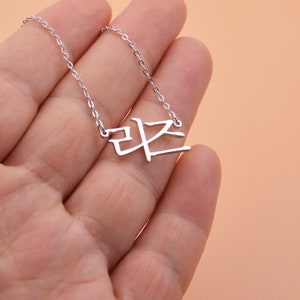 Pu&ograve; includere: Una collana d'argento con un ciondolo con un carattere coreano. Il ciondolo ha la forma del carattere coreano per "pace".