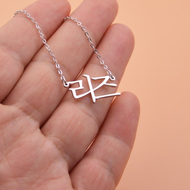 Pu&ograve; includere: Una collana d'argento con un ciondolo con un carattere coreano. Il ciondolo ha la forma del carattere coreano per "pace".