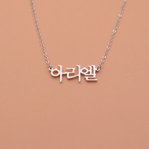 Pu&ograve; includere: Collana d'argento con la parola coreana "아리엘" appesa.