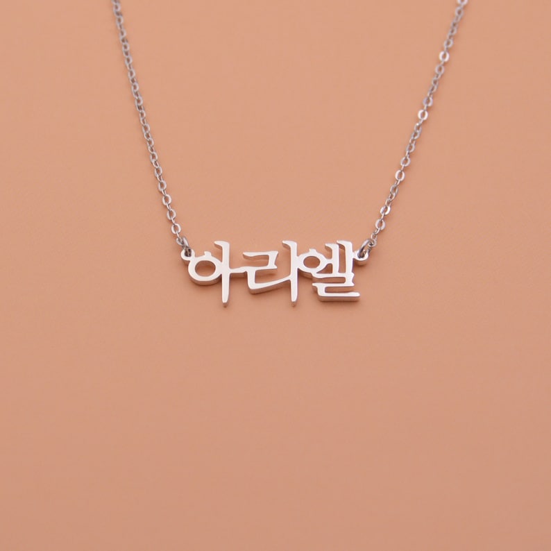 Pu&ograve; includere: Collana d'argento con la parola coreana "아리엘" appesa.