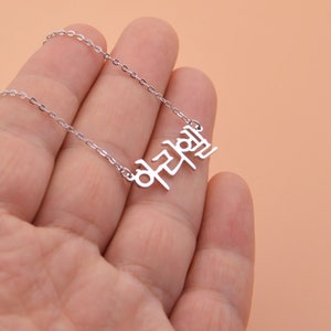 Pu&ograve; includere: Collana d'argento con un ciondolo con una parola coreana. La parola &egrave; "notevole" in coreano.