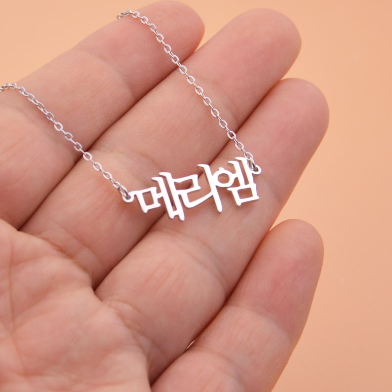 Pu&ograve; includere: Una collana d'argento con un ciondolo a forma di parola coreana che si legge "대한민국".