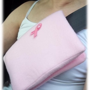 May include: Pink fleece seatbelt shoulder pad with a pink ribbon embroidered on the front.