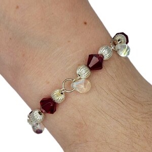 Op de afbeelding: Een zilveren en gouden armband met rode en heldere kristallen kralen.