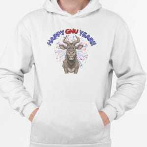 Puede incluir: Sudadera con capucha blanca con un diseño de ñu de dibujos animados y el texto "HAPPY GNU YEAR!!" en azul y rojo. El diseño presenta un ñu sonriente con fuegos artificiales y estrellas.