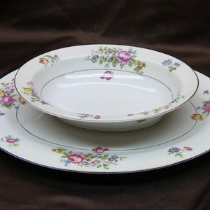 May include: A white oval serving dish with a floral pattern in shades of pink, yellow, and blue. The dish is nested inside a larger white oval platter with a similar floral pattern.