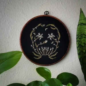 May include: A black embroidery hoop with a gold floral design on a black background. The design features stylized flowers and leaves.