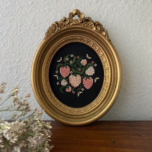 May include: A gold framed picture with a black background and a cross-stitch design of pink hearts and green leaves.