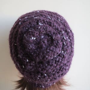 K&ouml;nnte beinhalten: Eine gestrickte M&uuml;tze in Lila und Wei&szlig; mit einem strukturierten Design.