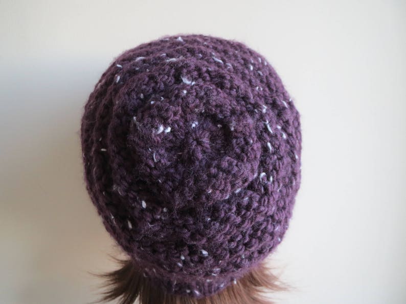 K&ouml;nnte beinhalten: Eine gestrickte M&uuml;tze in Lila und Wei&szlig; mit einem strukturierten Design.
