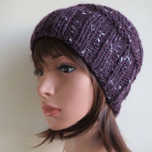 K&ouml;nnte beinhalten: Eine lilafarbene Strickm&uuml;tze mit wei&szlig;en Flecken. Die M&uuml;tze ist aus weichem, strukturiertem Garn gefertigt und hat eine lockere Passform.