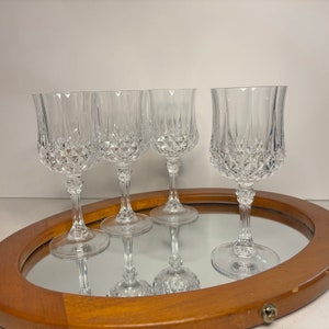 May include: Four clear glass wine glasses with a diamond pattern on a wooden tray with a mirror surface.