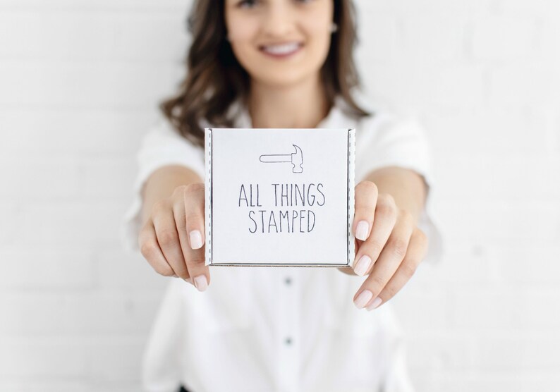 Op de afbeelding: Een witte doos met de tekst "ALL THINGS STAMPED" en een kleine afbeelding van een hamer.